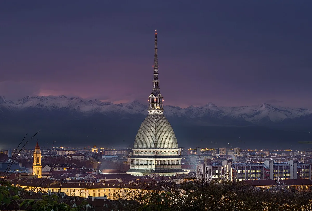 De Mole Antonelliana van Turijn verlicht bij avondschemering met de Alpen op de achtergrond